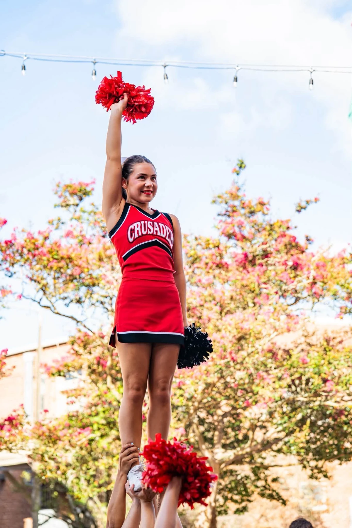 Cheerleader in red uniform being held up in air by others.
