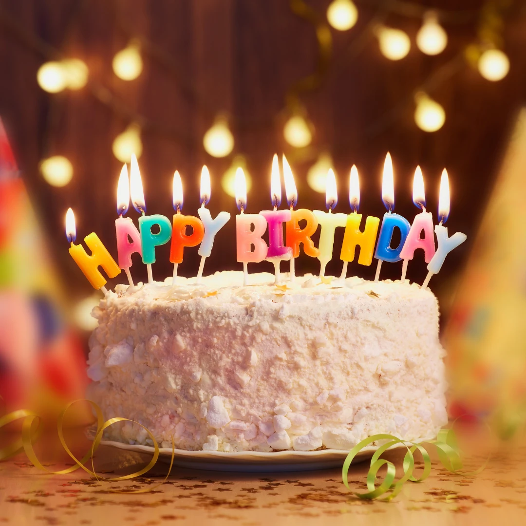 Birthday cake with candles, surrounded by festive elements, dim background.